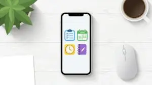 En smartphone på ett vitt skrivbord visar fyra färgglada ikoner: en blå checklista, en grön kalender märkt 2026, en gul klocka och en lila anteckningsbok. I närheten finns en växt, en kaffekopp, en vit mus och ett papper.